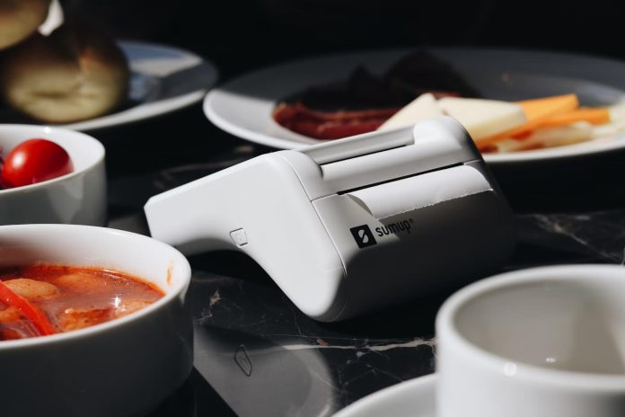 A portable SumUp card reader placed on a table among plates of food, symbolizing mobile payment solutions in small businesses and informal sectors.