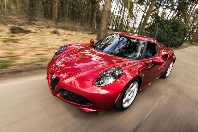 Red traditional sports car driving on a forest road.