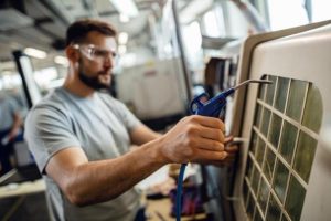 Technician cleaning an AC unit filter with a tool.
