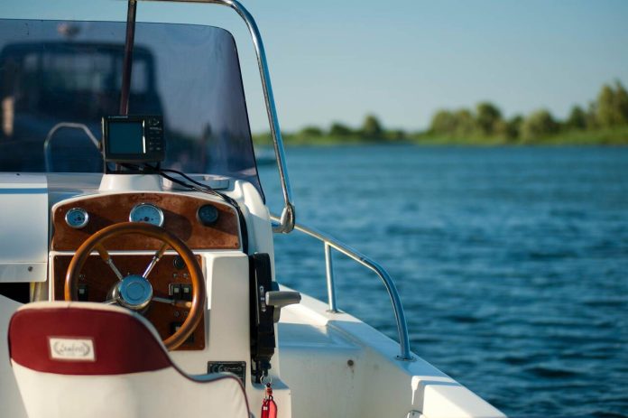 Helm of a yacht with a wooden steering wheel, navigational display, and a scenic water view in the background.