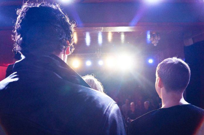 Speakers on stage under bright AV lights facing the audience.