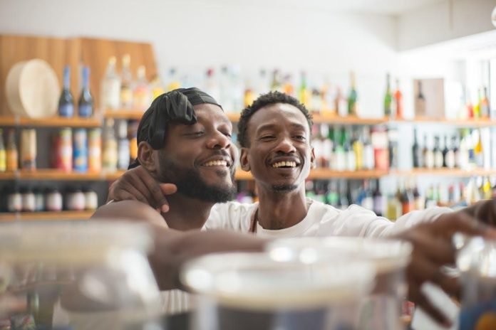 Two men smiling behind counter in a liquor store.