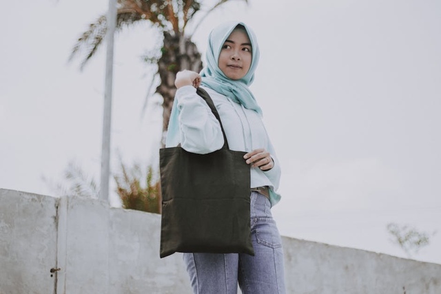 Young woman wearing a light hijab carrying a black tote bag outdoors in a minimalist fashion style